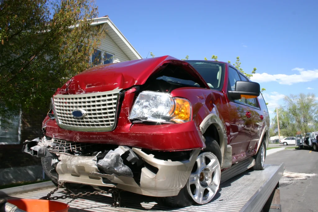 Damaged red SUV with front-end collision damage on a tow truck for auto body repair